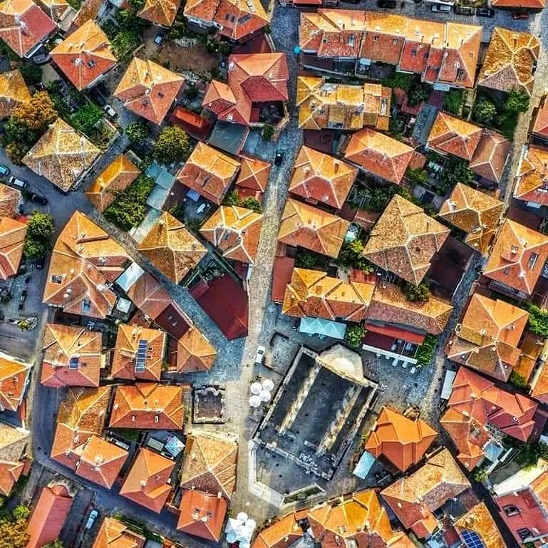 Nessebar Old Town from directly above: densely packed terracotta roofs, narrow cobbled lanes, and the roofless stone walls of an ancient basilica in the centre of the UNESCO-listed peninsula.